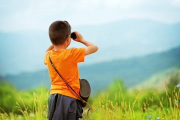 Little boy looking through binoculars outdoor. He is lost