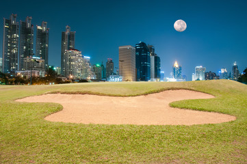 Sand bunker on the golf course with illuminated buildings on the