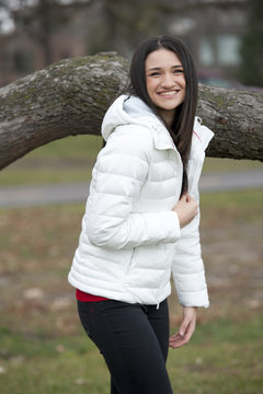 A young and happy brunette girl wearing a white puffy coat in the fall on a cloudy day.