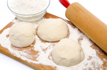 Three balls of pizza dough with a cup of flour and a rolling pin