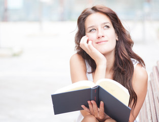 Thoughtful girl reading a book. In the city.