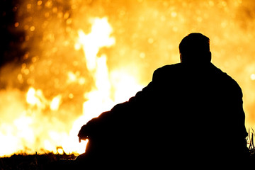 Mann sitzt vor Sonnwendfeuer