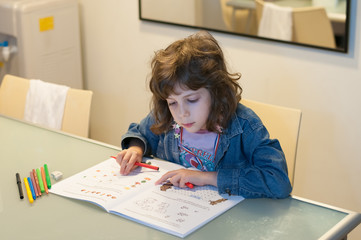 Little girl sitting at a table drawing and coloring in her book