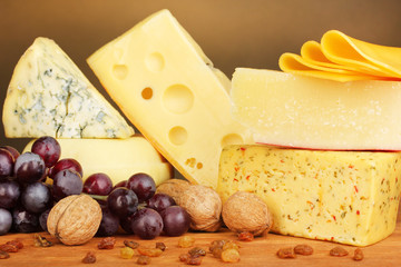 Various types of cheese on wooden table on brown background