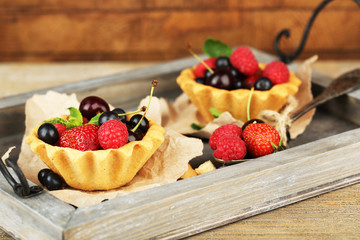 Tasty tartlets with berries on wooden tray
