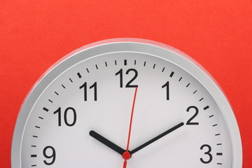 Fototapeta na wymiar Wall clock in half profile against a bright red paper background