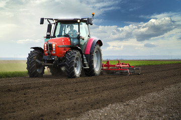 Obraz premium Close-up of agriculture red tractor cultivating field