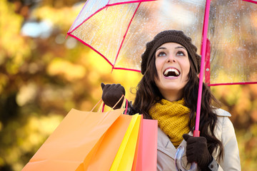 Woman holding shopping bags and umbrella in autumn