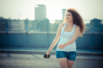 Smiling young woman listening to music while walking on street during sunset