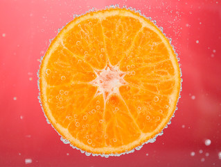 Fresh orange in water with bubbles on red background