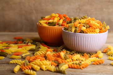 Assortment of colorful pasta in color bowls on wooden