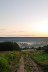 Obraz premium country road and fog over river in summer twilight