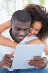 Attractive couple sitting on couch together looking at tablet