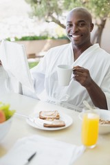Obraz na płótnie Canvas Handsome man in bathrobe having breakfast outside