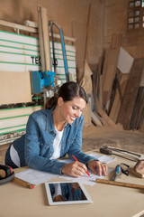 Female Carpenter Working On Blueprint In Workshop