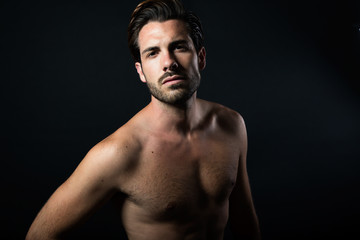 Fototapeta premium Handsome muscular male model posing over black background.