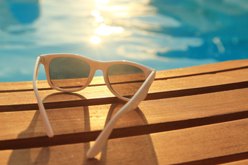 Sunglasses on wooden planks and water on sunset