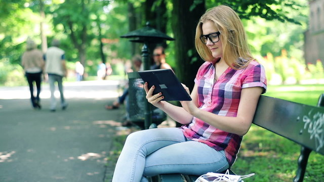 Young teenager with tablet computer sitting on bench in park