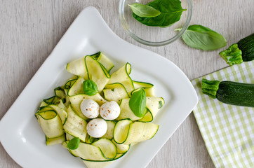 Fresh raw zucchini salad with basil and mozzarella wooden backgr