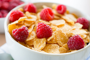 Cornflakes and red rasberries in a white bowl
