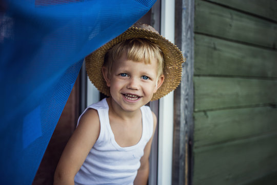 Cheerful kid with straw hat leaning out a window