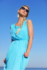 girl in a blue dress and sunglasses on background of sky