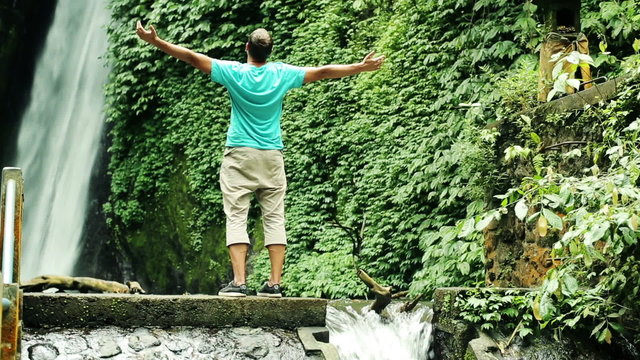 Man raising arms to the sky by beautiful waterfall in Bali
