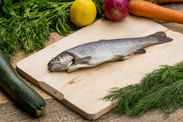 Fresh trout on a cutting board, fresh vegetables in the background