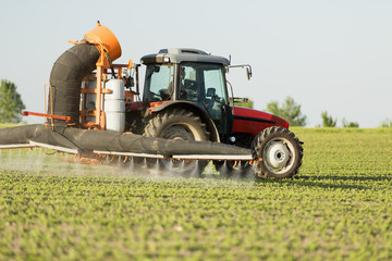 Tractor spraying soybean crops field with sprayer