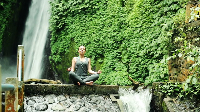 Young woman meditating by amazing waterfall in Bali, Indonesia