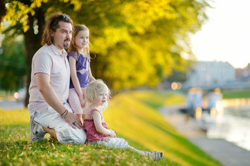 Fototapeta premium Young father and his daughters sitting by a river