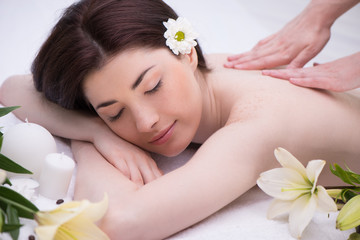 Obraz na płótnie Canvas Relaxed woman with flowers in spa center enjoying massage