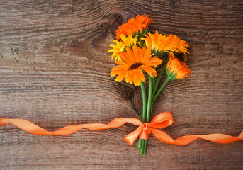 Bouquet from flowers of calendula with orange satin ribbon on wo - obrazy, fototapety, plakaty