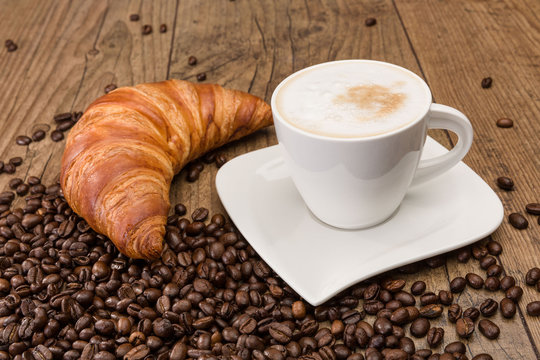 Tasse Cappuccino mit Croissant und Kaffeebohnen