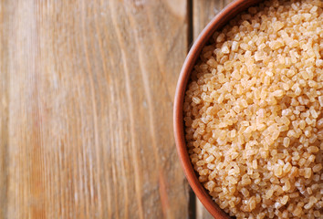 Brown crystal sugar in bowl on wooden background