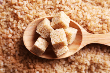Brown sugar cubes in wooden spoon on crystal sugar background