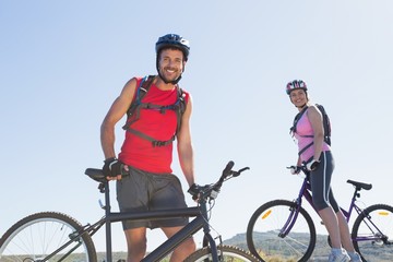 Fototapeta premium Fit cyclist couple standing at the summit smiling at camera