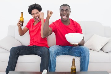 Football fans in red sitting on couch with beer and popcorn
