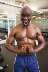 Fototapeta na wymiar Muscular man shouting while flexing muscles in gym