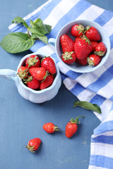 Ripe sweet strawberries in mugs  on color wooden background