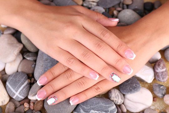 Female hand with stylish colorful nails on sea pebble