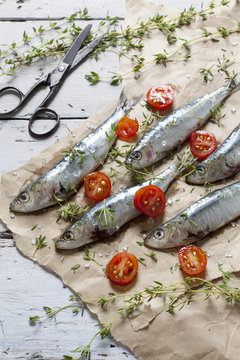 fresh sardines with tomatoes slices and thyme on brown paper