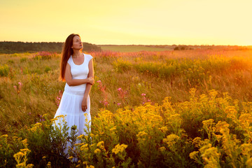 Fototapeta na wymiar Young woman in white clothes standing in field on sunset