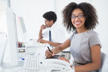 Young pretty designer smiling at camera at her desk