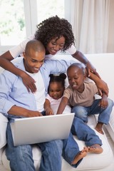 Happy family sitting on couch together using laptop