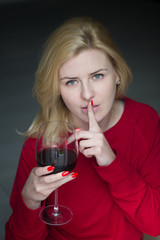 Woman drinking red wine with finger on mouth - secret