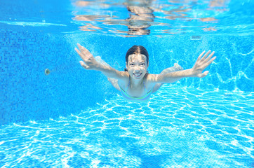 Happy underwater child swims in pool, girl swimming