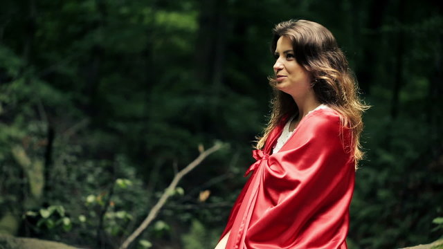 Happy beautiful woman, red riding hood sitting in the forest