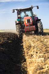 Farmer plowing stubble field with red tractor