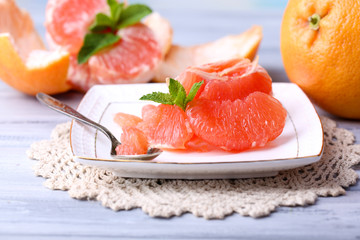 Ripe peeled grapefruits on plate, on color wooden background
